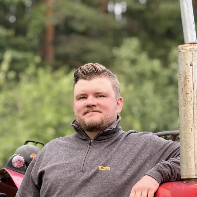 Eetu Tervo, founder of ISOBUS Block, leaning on a tractor in a Block-branded jacket